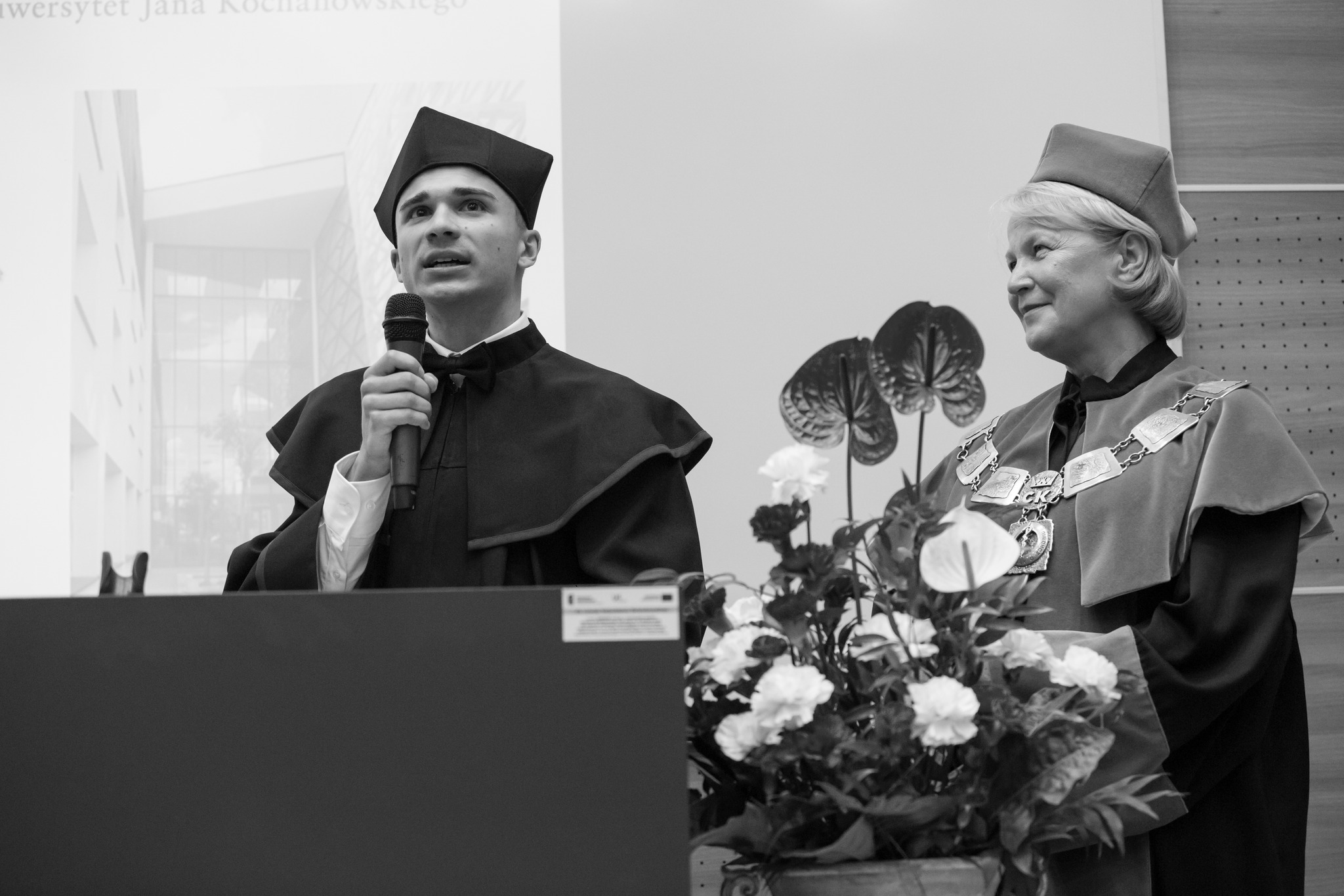 Absolwent Damian Zaręba przemawia i Pani Dziekan Janion z kwiatami na auli