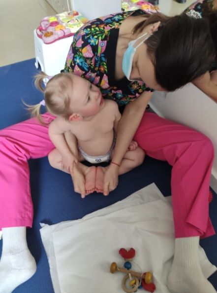 Fizjoterapeuta siedzi z dzieckiem na podłodze, widać zabawki dziecięce